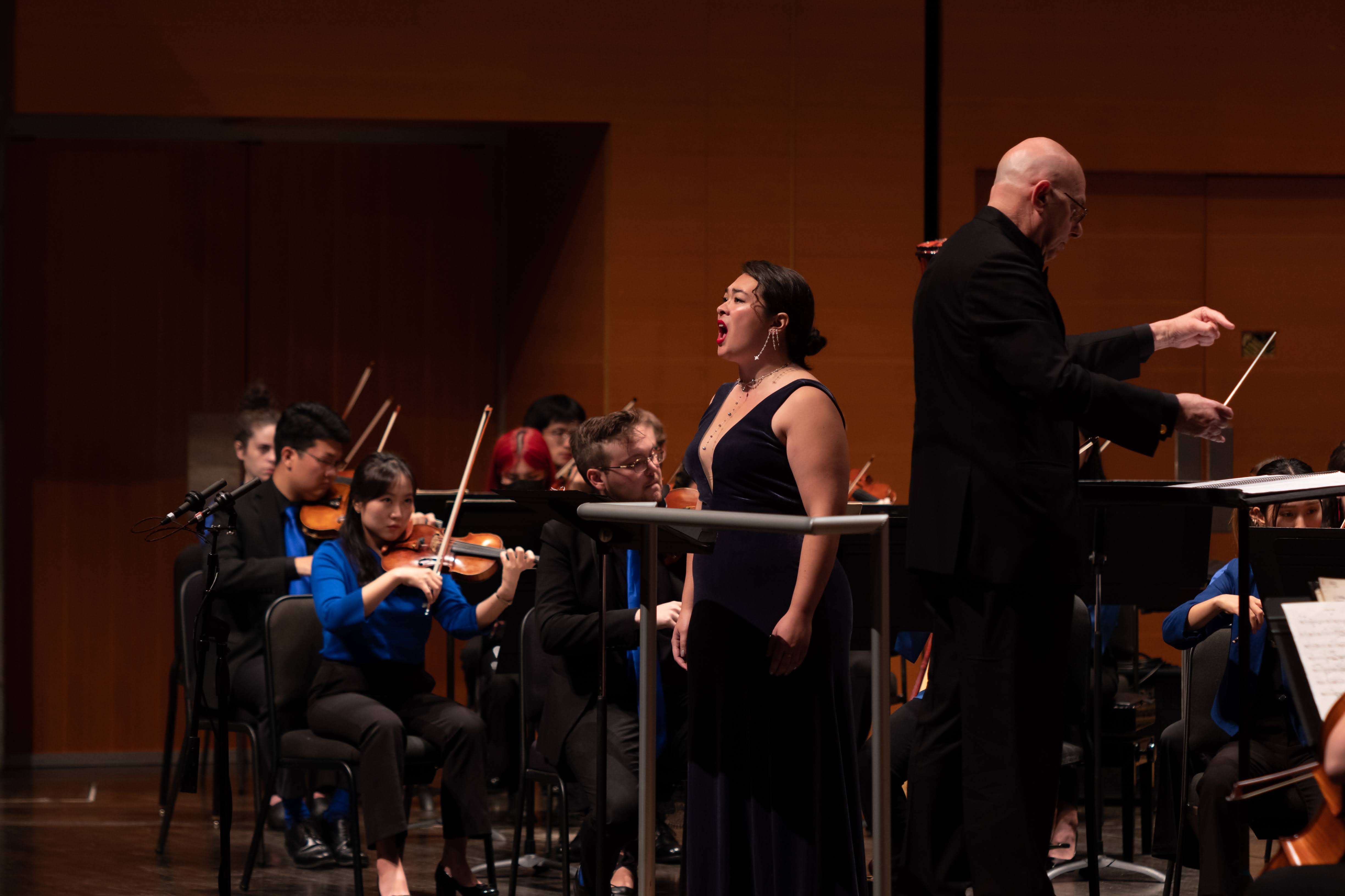 Leon Botstein conducts while a soloist sings next to him in a black dress.